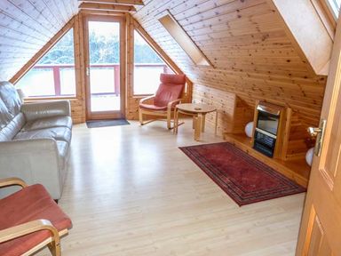 A living room with wooden walls a sofa chairs and a rug at Strathavon Chalet in Aviemore