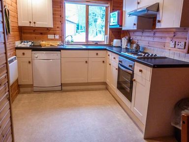 A kitchen with white cabinets dishwasher oven stovetop microwave and window at Strathavon Chalet in Aviemore