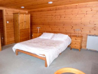 A bedroom with a double bed a wooden wardrobe two bedside tables with lamps and wooden walls at Strathavon Chalet in Aviemore