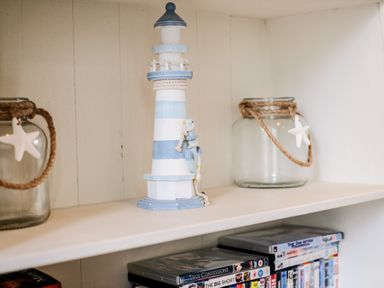 A shelf with a blue and white lighthouse decoration glass jars with rope and starfish and dvd cases at Stones Throw in Charlestown
