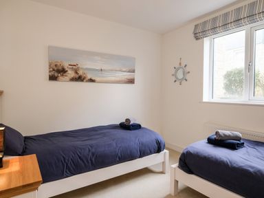 A bedroom with two single beds with navy bedding towels on beds a window and painting on wall at Stones Throw in Charlestown