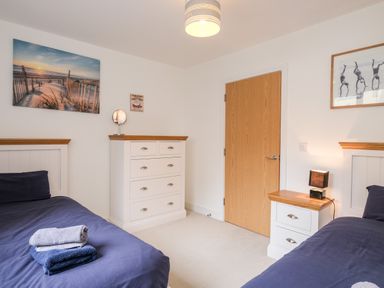 A bedroom with two single beds with navy covers a chest of drawers a nightstand and wall art at Stones Throw in Charlestown