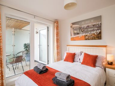 A bedroom with a double bed orange pillows folded towels balcony chairs and a wall art at Stone's Throw in Charlestown