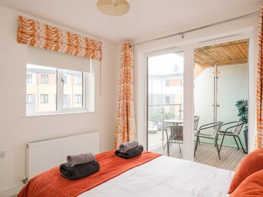 A bedroom with orange and white curtains two windows a bed with folded towels and a balcony with chairs and a table at Stones Throw in Charlestown