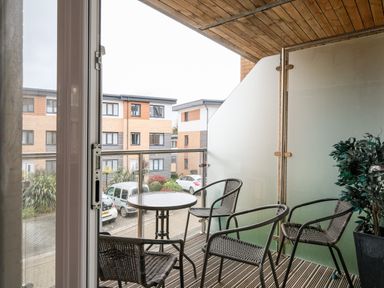 A balcony with four woven chairs and a round table overlooking cars and buildings at Stone's Throw in Charlestown