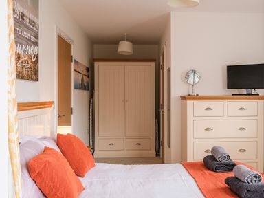 A bedroom with a bed with orange pillows and blanket a wardrobe and a dresser with a mirror and tv at Stone's Throw in Charlestown