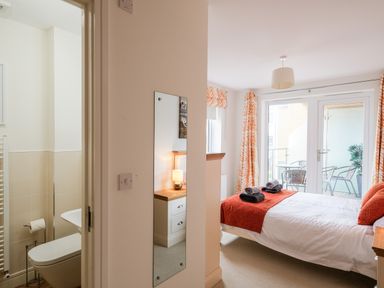 A bedroom with a bed folded towels bedside table and lamp next to a bathroom and balcony doors at Stone's Throw in Charlestown