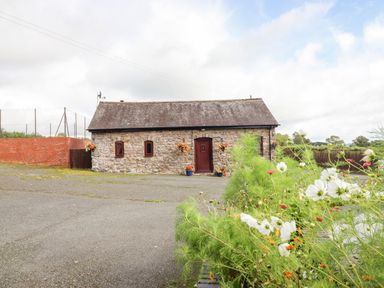 A stone building with a shingled roof and a red door with flowers in pots outside at Bwthyn Ty Newydd in Llangadfan