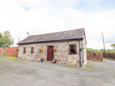 A stone cottage with a wooden door and four windows surrounded by flower pots and hanging planters at Bwthyn Ty Newydd in Llangadfan