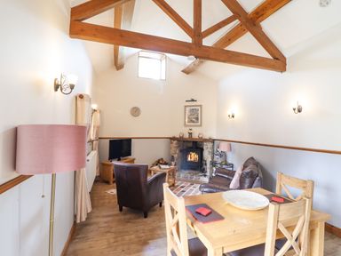 A living room with wooden ceiling beams a fireplace two chairs a sofa a dining table and a floor lamp at Bwthyn Ty Newydd in Llangadfan
