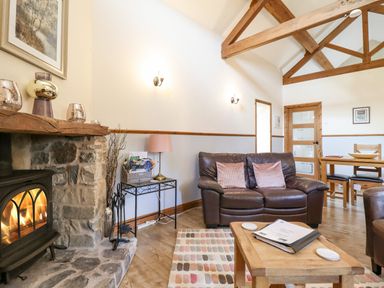 A living room with a stone fireplace, brown leather sofa, wooden coffee table, and dining table at Bwthyn Ty Newydd in Llangadfan