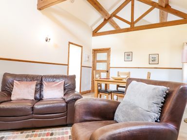 A living room with brown leather sofa and armchair with cushions and a wooden dining table with chairs at Bwthyn Ty Newydd in Llangadfan