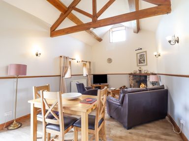 A dining table with four chairs and a living area with leather sofas and a fireplace at Bwthyn Ty Newydd in Llangadfan