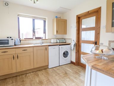 A kitchen with wooden cabinets a microwave kettle toaster dishwasher washing machine and a glass cake stand at Bwthyn Ty Newydd in Llangadfan