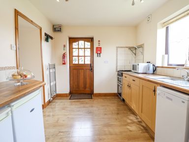 A kitchen with wooden cabinets appliances and a wooden door at Bwthyn Ty Newydd in Llangadfan