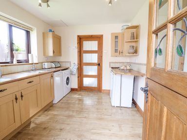 A kitchen with wooden cabinets a washing machine a dishwasher and a wooden door at Bwthyn Ty Newydd in Llangadfan