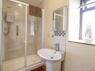 A bathroom with a shower enclosure a pedestal sink a mirror with lights and a window at Bwthyn Ty Newydd in Llangadfan