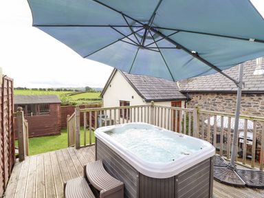 An outdoor deck with a hot tub under a blue umbrella and a wooden fence with green fields in the background at Bwthyn Ty Newydd in Llangadfan