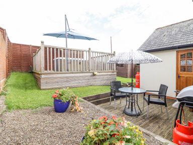 An outdoor patio with a table and chairs under an umbrella next to a building with a wooden door and a hot tub on a raised deck with a large umbrella at Bwthyn Ty Newydd in Llangadfan