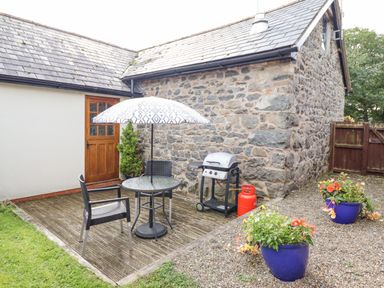 An outdoor patio area with a glass table umbrella two chairs a barbecue grill and flower pots at Bwthyn Ty Newydd in Llangadfan