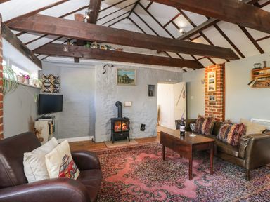 A living room with exposed wooden beams a wood stove a patterned rug leather sofas and a wooden coffee table at Old Cart Shed Lyneham near Royal Wootton Bassett