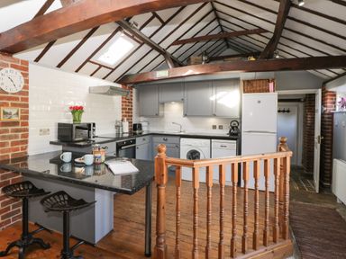 A kitchen with grey cabinets black countertops wooden floor and two stools at Old Cart Shed in Lyneham near Royal Wootton Bassett