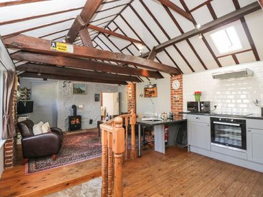 An open plan kitchen and living area with exposed beams a wood stove and wooden floor at Old Cart Shed in Lyneham near Royal Wootton Bassett
