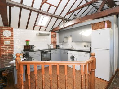 A kitchen with wooden beams a washing machine dishwasher gray cabinets and a white fridge at Old Cart Shed Lyneham near Royal Wootton Bassett