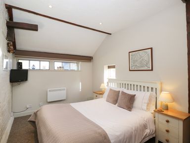 A bedroom with a double bed two bedside tables and small windows at Old Cart Shed Lyneham near Royal Wootton Bassett