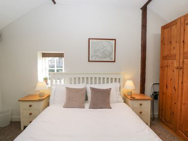 A bedroom with a white bed with two pillows two bedside tables with lamps a wooden wardrobe and a framed map on the wall at Old Cart Shed in Lyneham near Royal Wootton Bassett