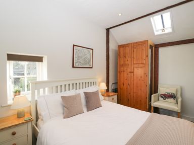 A bedroom with a white bed two bedside tables with lamps a wooden wardrobe and a chair at Old Cart Shed Lyneham near Royal Wootton Bassett