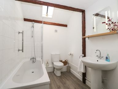 A bathroom with a bathtub shower toilet sink mirror and wooden shelf at The Old Cart Shed in Lyneham near Royal Wootton Bassett