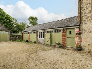 A courtyard with green doors on a stone and brick building at The Old Cart Shed Lyneham near Royal Wootton Bassett