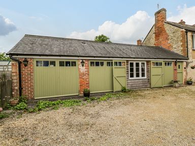 A gravel driveway with green garage doors attached to a stone and brick building at Old Cart Shed Lyneham near Royal Wootton Bassett
