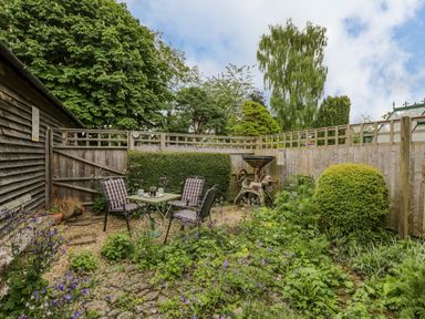 A garden patio with a table and four chairs surrounded by plants and a wooden fence at Old Cart Shed in Lyneham near Royal Wootton Bassett