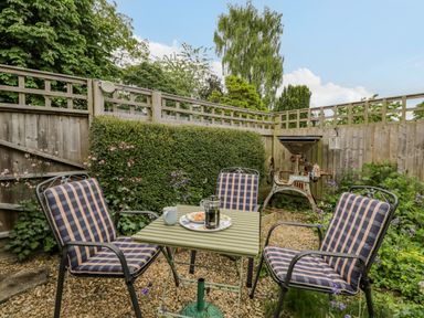 A small garden patio with a green table and four cushioned chairs surrounded by plants and wooden fencing at The Old Cart Shed in Lyneham near Royal Wootton Bassett