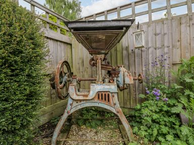 An old rusty metal machine in a corner garden surrounded by wooden fencing and plants at The Old Cart Shed in Lyneham near Royal Wootton Bassett