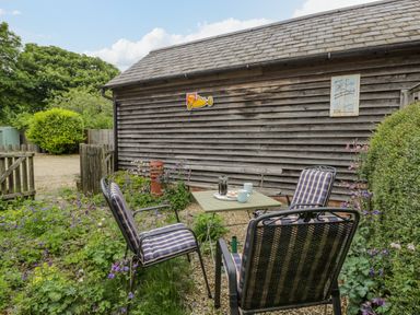 An outdoor seating area with four cushioned chairs and a small table next to a wooden shed surrounded by plants and flowers at Old Cart Shed in Lyneham near Royal Wootton Bassett