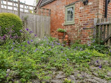 A garden with purple flowers near a brick wall and wooden fence at Old Cart Shed in Lyneham near Royal Wootton Bassett