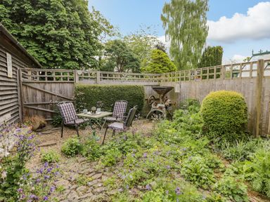 A garden area with a table and three chairs surrounded by plants and a wooden fence at Old Cart Shed Lyneham near Royal Wootton Bassett