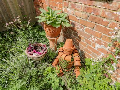 A garden corner with potted plants and a figure made of terracotta pots against a brick wall at Old Cart Shed in Lyneham near Royal Wootton Bassett