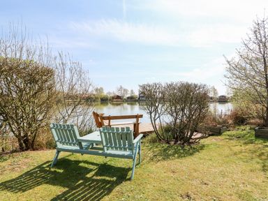 A garden area with two benches and a wooden dock by a lake at Bittern Lodge in Tattershall Lakes Country Park