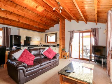 A living room with a brown leather sofa and kitchen area with white cabinets and black appliances at Bittern Lodge in Tattershall Lakes Country Park