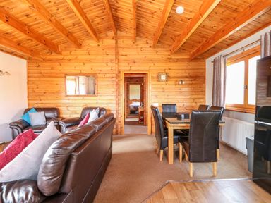A wooden interior living room with leather sofas and a dining table with chairs at Bittern Lodge in Tattershall Lakes Country Park
