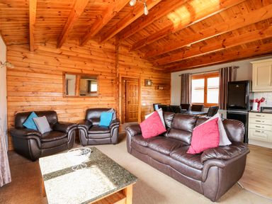 A living room with brown leather sofas and colorful cushions a wooden coffee table and dining area with black chairs at Bittern Lodge in Tattershall Lakes Country Park