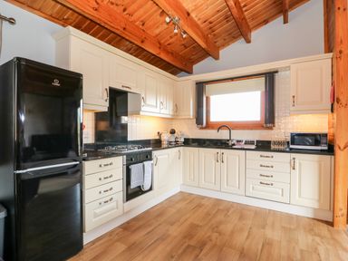 A kitchen with cream cabinets black appliances and a wooden ceiling at Bittern Lodge in Tattershall Lakes Country Park