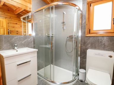 A bathroom with a corner shower enclosure a white vanity with drawers a toilet a window and wooden paneling at Bittern Lodge in Tattershall Lakes Country Park