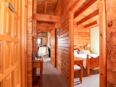 A wooden hallway leading to a bedroom with a bed and bedside table at Bittern Lodge in Tattershall Lakes Country Park