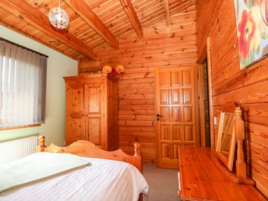 A bedroom with wooden bed frame wooden wardrobe wooden dresser with mirror and vertical blinds on the window at Bittern Lodge in Tattershall Lakes Country Park