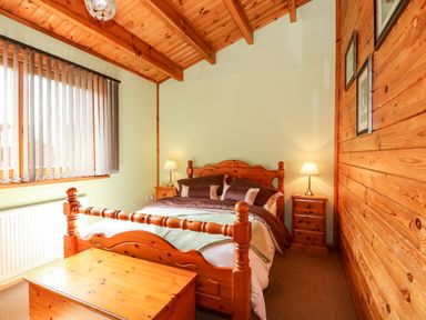 A bedroom with wooden bed frame bedside tables lamps and a chest at Bittern Lodge in Tattershall Lakes Country Park